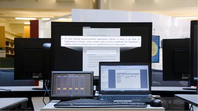 Picture of a large monitor in the back and 2 smaller monitors and a key board sitting on a desk.