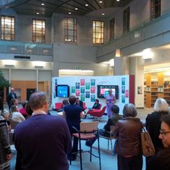 A picture of a crowd listening to a presenter who is standing in front of one panel of the Hub.